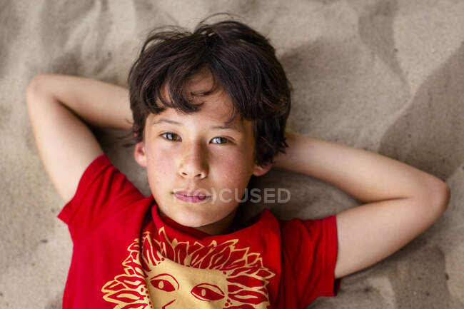 Close-up portrait of beautiful boy with bright eyes laying on beach — Stock Photo