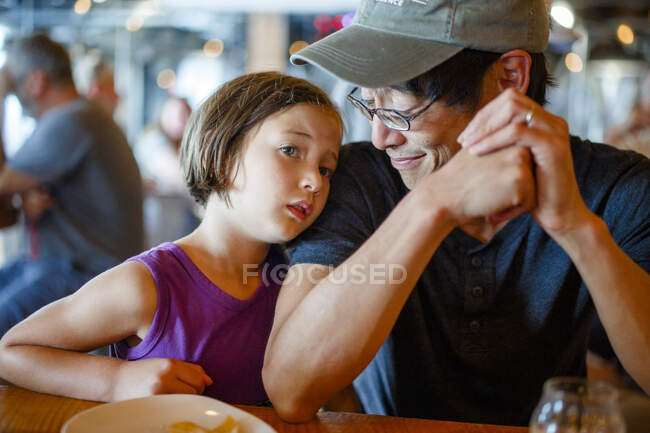 A father smiles down at child leaning on him in crowded restaurant — Stock Photo