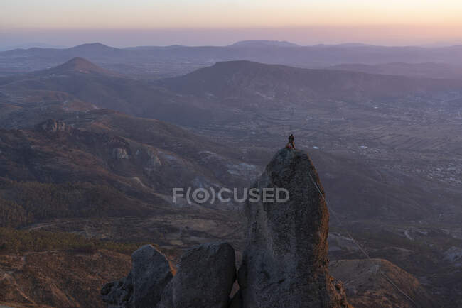 Un hombre parado en la parte superior de una roca expuesta alta fijando un slickline - foto de stock