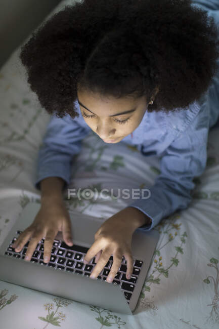 Elfjähriges zweirassiges Mädchen arbeitet auf Laptop im Bett — Stockfoto