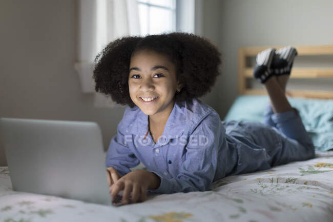 Onze anos de idade bi-racial menina trabalhando no laptop na cama — Fotografia de Stock