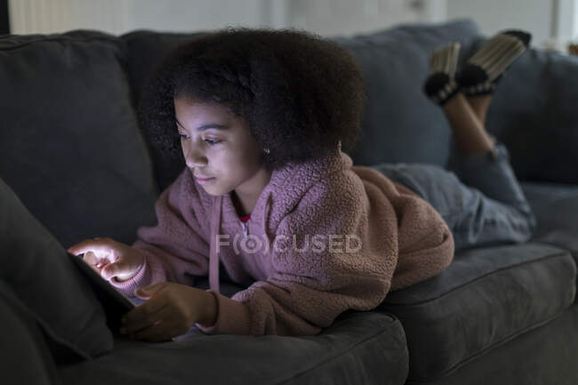 Dez anos de idade bi-racial menina trabalhando em seu ipad enquanto deitado no sofá — Fotografia de Stock