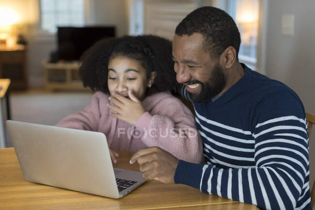 African-American father and tween daughter laugh looking at laptop — Stock Photo