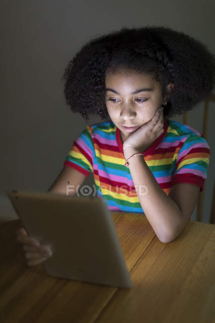10-jähriges zweirassiges Mädchen schaut auf iPad am Tisch — Stockfoto