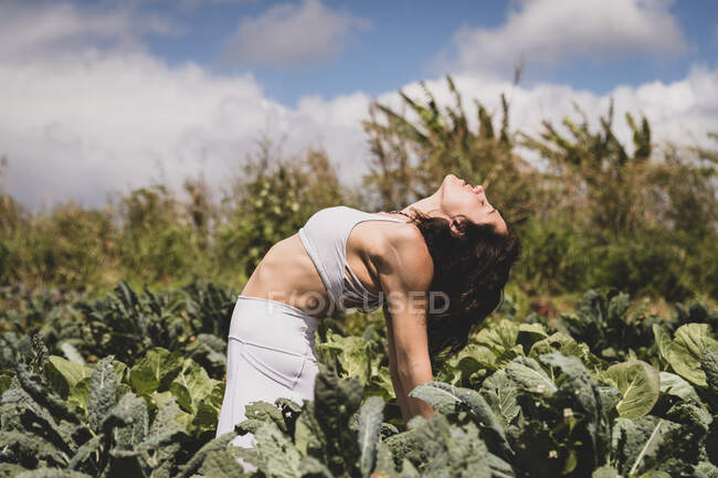 Female yogi backbends in field of vegetables — Stock Photo