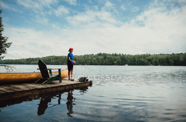 Adolescente pescando desde un muelle en un lago tranquilo en el verano. - foto de stock