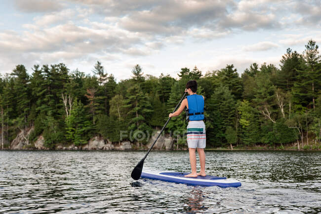 Jeune garçon pagayant sur un SUP sur un lac en Ontario, Canada par une journée ensoleillée. — Photo de stock
