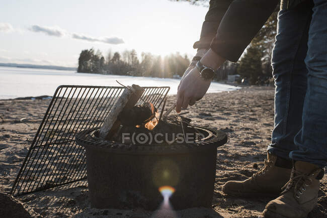 Mãos de homem acendendo uma fogueira fora em uma praia na Suécia — Fotografia de Stock