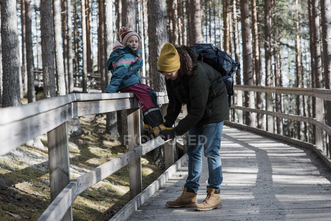 Padre ayudando a su hija a ponerse el zapato mientras camina en el bosque - foto de stock