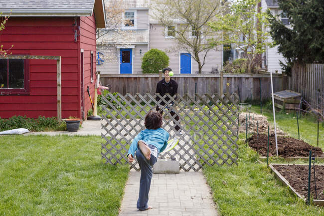 A boy and his father play makeshift tennis in yard over wood fencing — Stock Photo