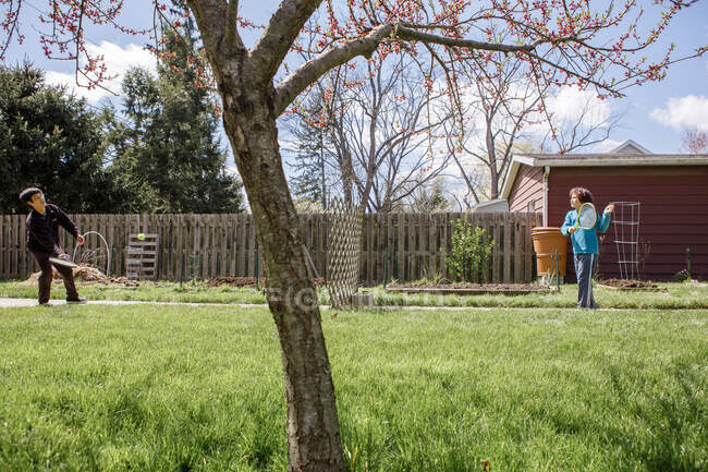 A father and son play tennis over a wooden fence in a garden in spring — Stock Photo