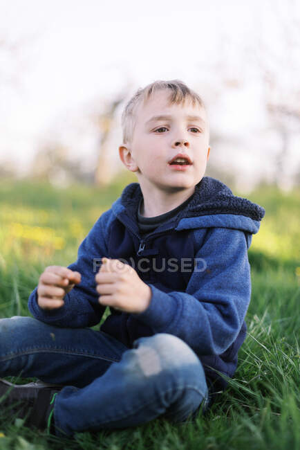 Мальчик, сидящий на траве и одуванчике. — стоковое фото
