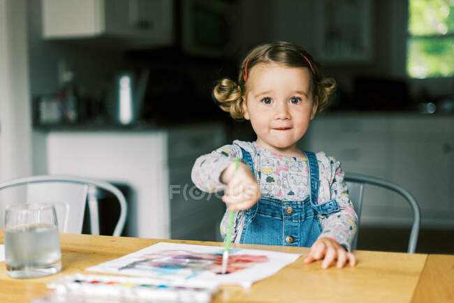 Une petite fille peignant avec des aquarelles à une table — Photo de stock