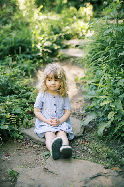Una bambina seduta su un gradino di pietra che guarda un fiume — Foto stock