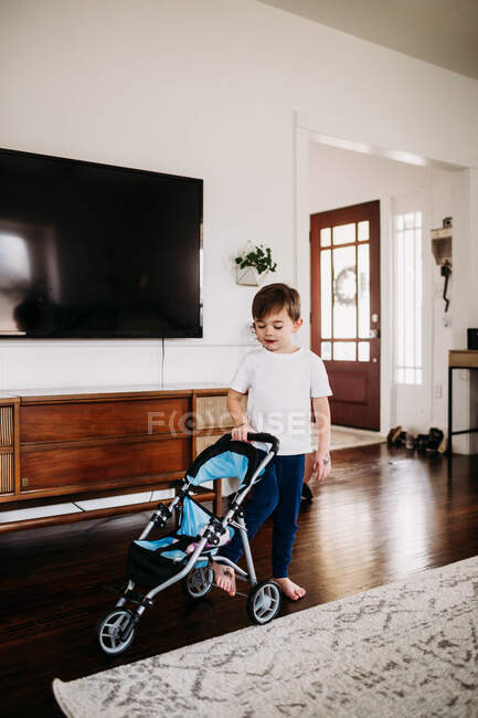 Jeune garçon poussant une poussette jouet dans le salon — Photo de stock