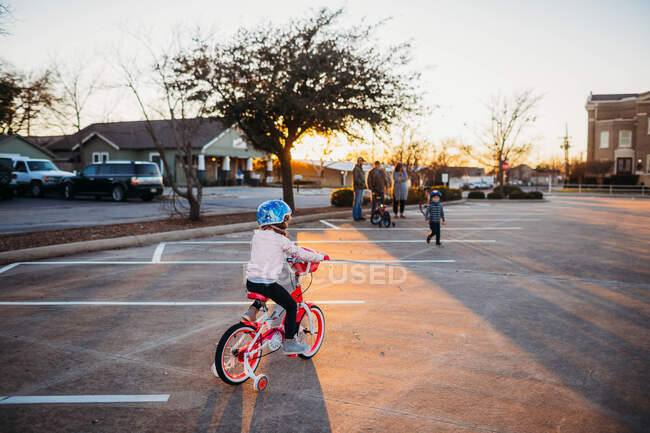 Junges Mädchen fährt auf dem Parkplatz mit dem Fahrrad auf Familie zu — Stockfoto