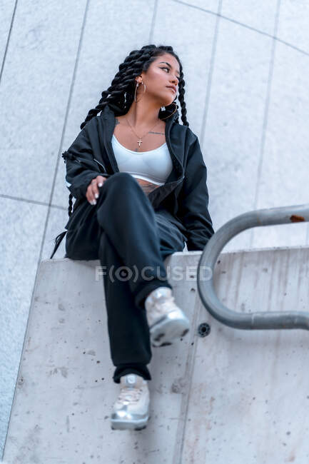 Молода чорна жінка сидить з косами, дивлячись праворуч сидячи — стокове фото