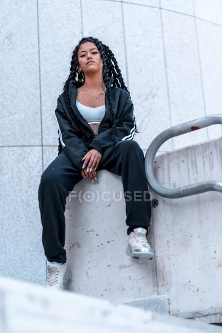 Молодая черная женщина сидит с косичками и татуировками, сидя — стоковое фото