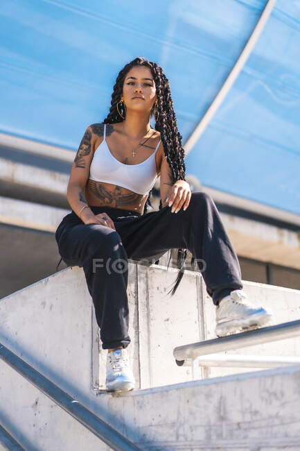 Joven chica negra con tatuajes, bailarina trampa sentada en la ciudad - foto de stock