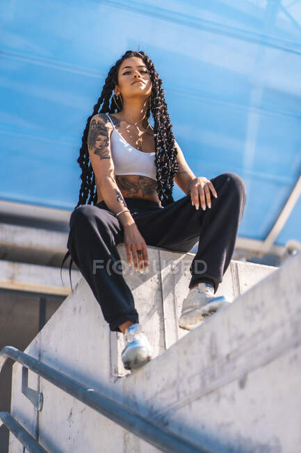 Молода чорна дівчина з татуюваннями, танцівниця пастки сидить на зупинці — стокове фото