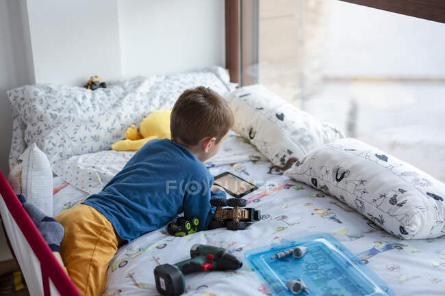 Ребенок, удобно лежащий в постели, делает видеозвонок — стоковое фото