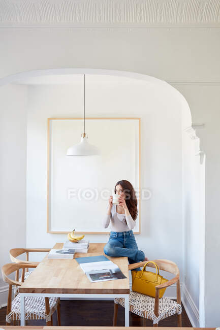 Жінка п'є каву на кухонному столі — стокове фото
