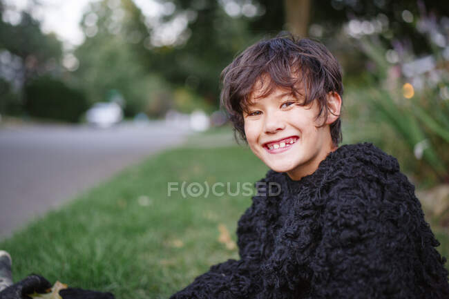 Um menino feliz em um terno de gorila sorri e senta-se em um quintal gramado — Fotografia de Stock