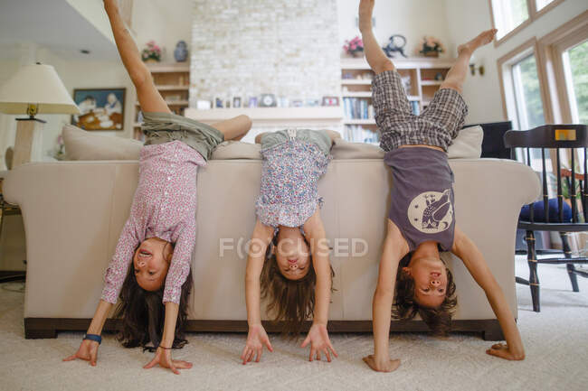 Three children lean against couch in living room doing handstands — Stock Photo