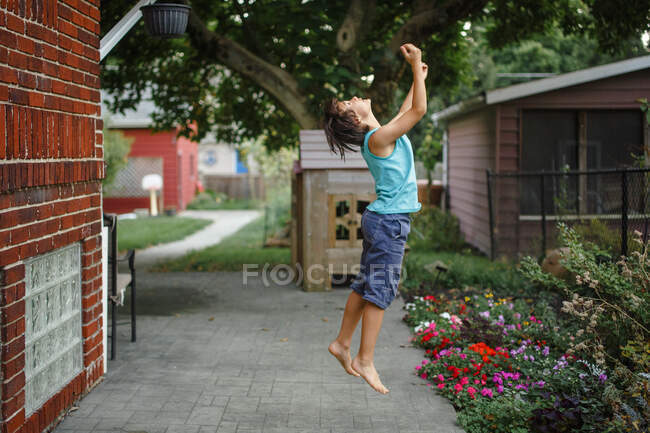 Молодий хлопчик підстрибує в повітря з руками, витягнутими в красивому саду — стокове фото