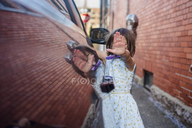 Uma menina refletida no lado do carro segura a mão na frente da cara — Fotografia de Stock