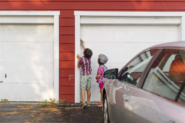 Двоє маленьких дітей стоять разом і натискають клавіатуру, щоб увійти в гараж — стокове фото