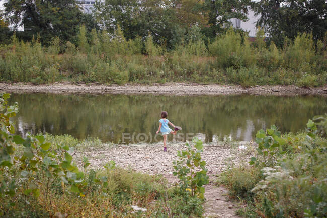 Distant view of girl standing on shore of river balancing on one leg — Stock Photo