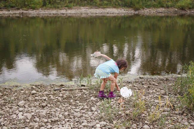 A little girl cleans litter up off of the shoreline of a river — Stock Photo