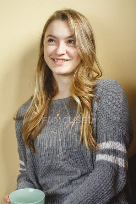 Молода жінка з носовим кільцем спирається на стіну всередині посміхаючись — стокове фото