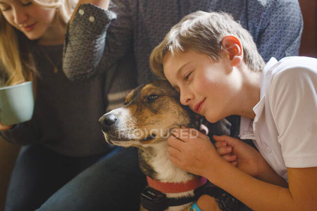 A tween boy sitting with siblings, leans his cheek against a dog — Stock Photo