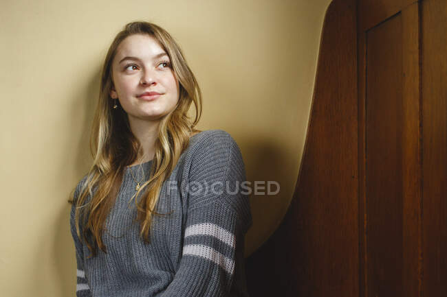 Drinnen sitzt eine junge Frau auf einer Holzbank und blickt in die Ferne — Stockfoto