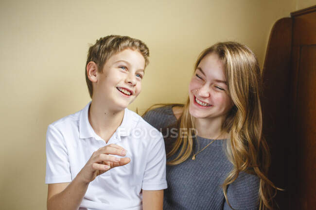 Two siblings sit together on a wood bench laughing with joy indoors — Stock Photo