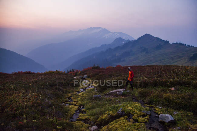 Contre un ciel coloré au lever du soleil, un grimpeur marche à travers un champ tout en montant vers Glacier Peak dans le Glacier Peak Wilderness à Washington. — Photo de stock