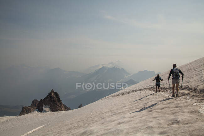 Zwei Bergsteiger steigen nach der Besteigung des Glacier Peak in der Glacier Peak Wilderness in Washington von einem Schneefeld ab. (veröffentlicht: Sam Thompson und Brock Gavery) — Stockfoto