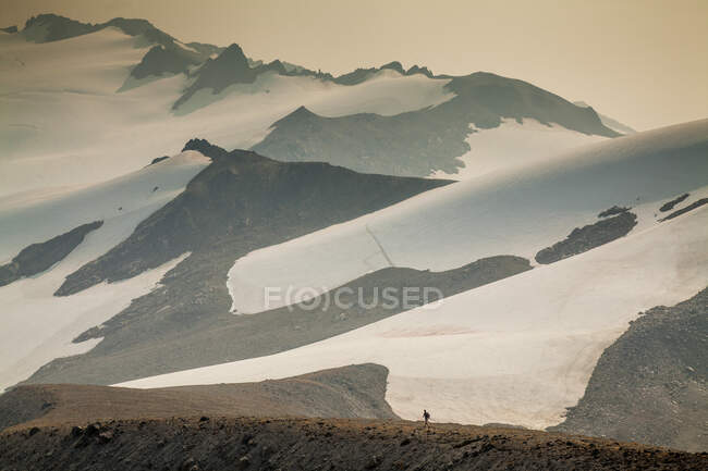 A lone climber ascends a trail on a ridge with the dramatic glaciers of Glacier Peak in Washington in the background. (released: Sam Thompson) — Stock Photo
