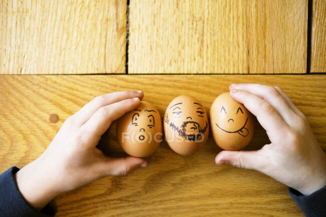 Little children hands holding on to funny Easter eggs with faces — Stock Photo