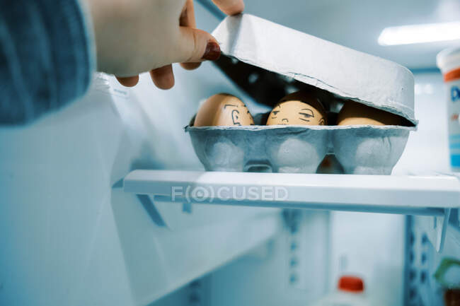 Коробка с яйцами в холодильнике с глупыми лицами, нарисованными на них для пасхального веселья — стоковое фото