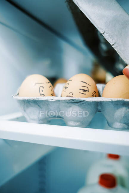 Коробка с яйцами в холодильнике с глупыми лицами, нарисованными на них для пасхального веселья — стоковое фото