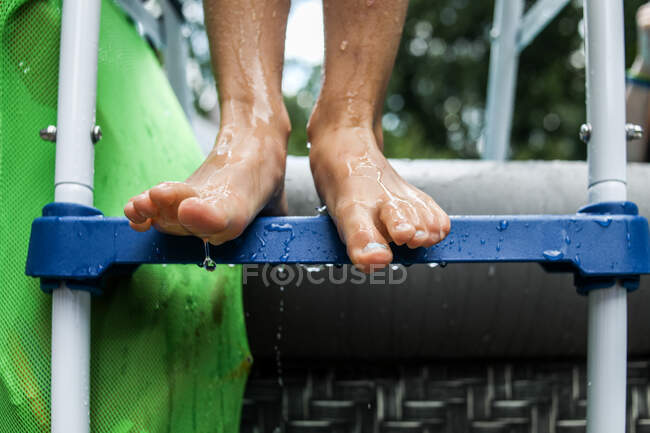 Gros plan des pieds mouillés debout sur l'échelle de la piscine avec de l'eau qui coule — Photo de stock