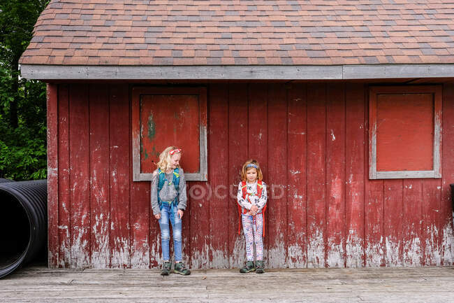 Two girls standing together against weathered red barn wall — Stock Photo