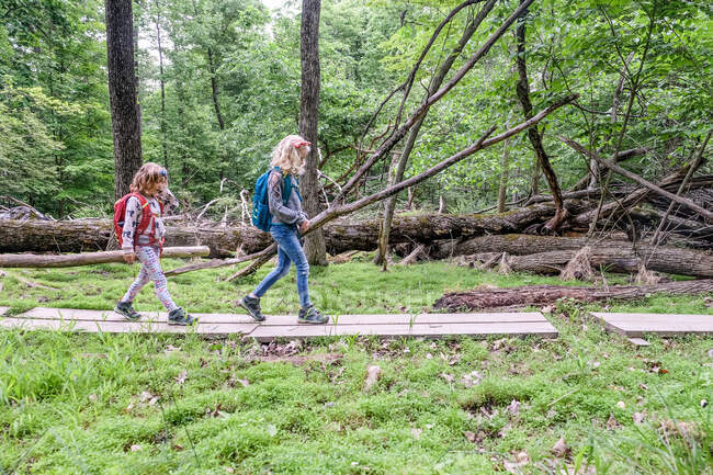 Two girls walking across wood planks while hiking together in spring — Stock Photo