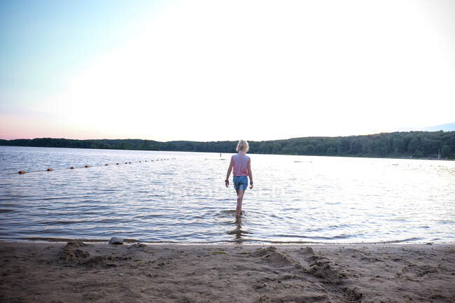 Girl walking into water at lake at sunset — Stock Photo