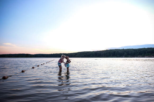 Дві дівчини грають у воді на озері на заході сонця влітку — стокове фото