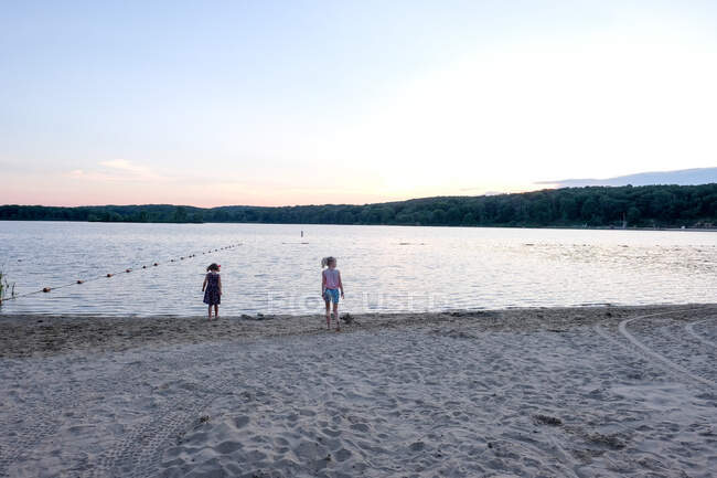 Two girls standing on shoreline of lake at sunset in sumemrtime — Stock Photo