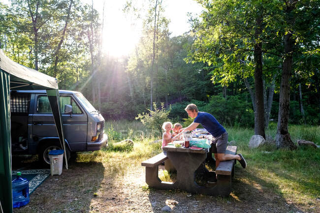 Familia sentados juntos en la cena mientras acampan en el bosque en verano - foto de stock